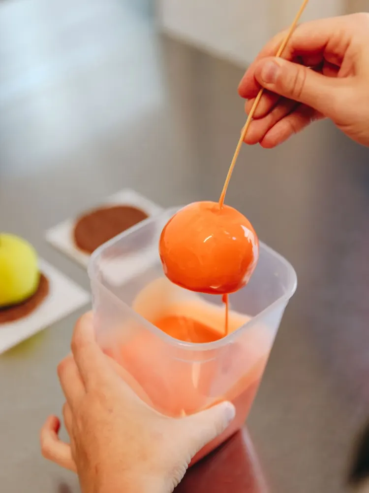 Un dolce a forma di frutto appena immerso nella glassa arancione, tenuto con uno stecco